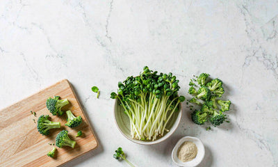 Overhead flat lay of broccoli sprouts, chopped broccoli florets and a bowl of mustard powder on marble