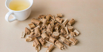 Bright flat-lay of licorice root pieces and a plain tea cup on a soft neutral surface, daily botanical
