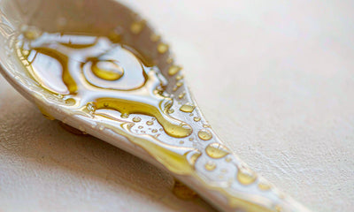 Macro close-up of golden olive oil droplets beading on a pale ceramic spoon in soft light
