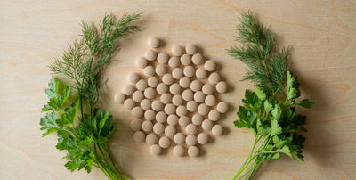 Flat lay of plain supplement pills with fresh green herbs on a bright light wood table in daylight