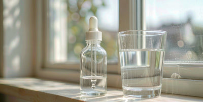 Macro of a plain glass dropper bottle and water glass on a bright windowsill, glutathione support