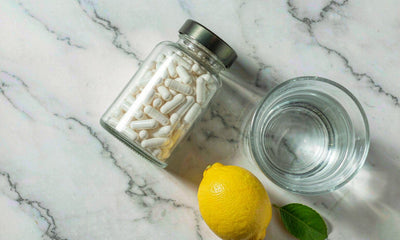 Bright flat-lay of a plain unlabeled supplement jar, a lemon, and water on marble for daily liver support.
