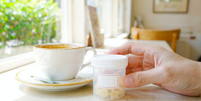 A hand holding a supplement gummy bottle at a bright cafe table beside a coffee cup
