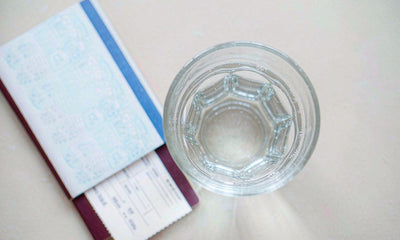 Open passport and boarding pass beside a glass of water on a bright hotel table, travel liver care.