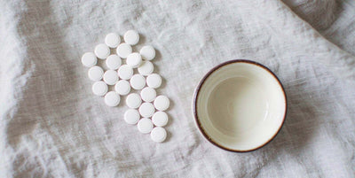 Flat-lay of plain unlabeled supplement tablets on a bright airy linen surface in daylight