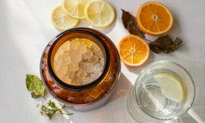 Plain unlabeled amber gummy jar with citrus slices and a glass of water on a bright white table overhead