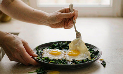 Fair-skinned hands preparing a plate of eggs and greens on a bright kitchen counter
