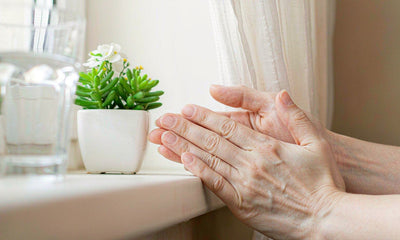Mature hands resting on a bright windowsill beside a glass of water and a small plant