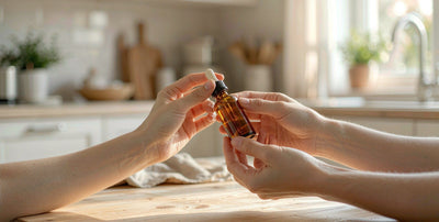 Fair-skinned hands holding a plain unlabeled supplement dropper bottle on a sunlit kitchen table