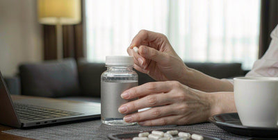 Western fair-skinned hands arranging a water bottle and supplement on a bright desk