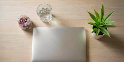 Top-down flat-lay of a plain supplement gummy jar, laptop, and plant on a bright desk for daily liver support.