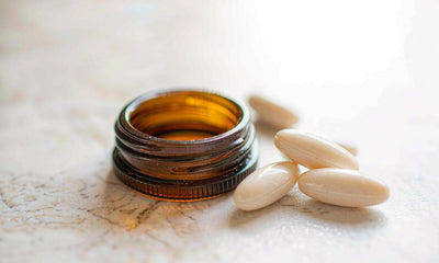 A plain unlabeled amber supplement bottle with pale capsules on a bright marble surface