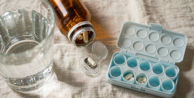 Amber supplement bottle with a pill organizer and water on a light linen tablecloth
