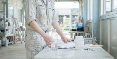 A worker seen from behind at a site table with a water bottle and a plain supplement jar