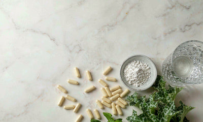Overhead flat lay of golden capsules, milk thistle leaves and dandelion greens on marble