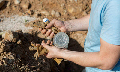Work gloves and a water bottle held in a worker's hands on a bright worksite