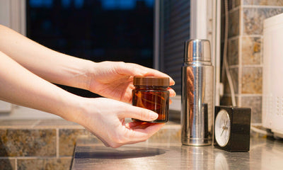 Hands holding a plain amber glass jar on a kitchen counter late at night