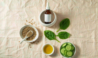 Overhead flat lay of an amber dropper bottle, lentils, spinach, cucumber and olive oil on linen
