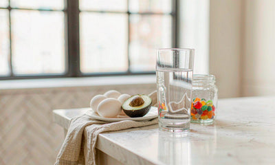Bright morning kitchen counter with water, a gummy jar, eggs and avocado in soft window light