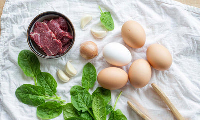 Overhead flat-lay of eggs, greens, and beef slices on white linen, whole-food protein for daily repair