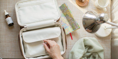 Open travel suitcase with a small supplement dropper bottle and a fair-skinned hand on a sunny hotel desk