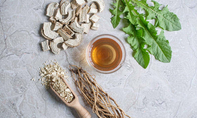 Flat lay of dried dandelion root, root shavings and a glass cup of amber tea