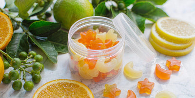 Plain unlabeled gummy supplement jar beside citrus slices and greens on light marble