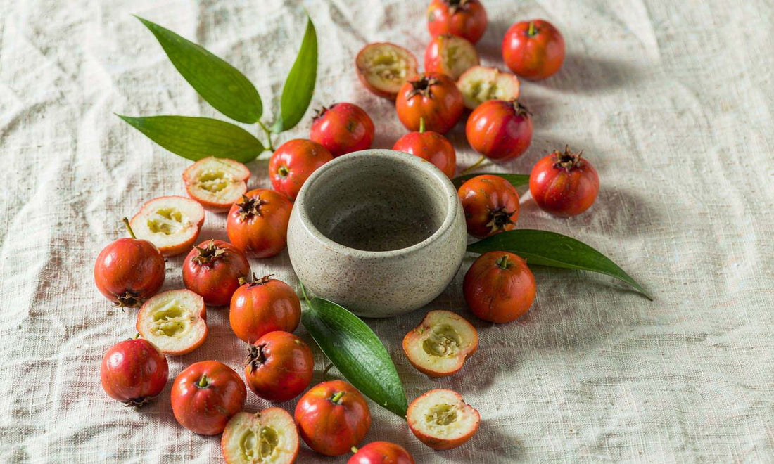 Deep red hawthorn berries and green leaves scattered with a small ceramic bowl on pale linen cloth