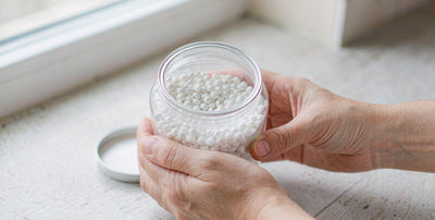 Fair-skinned hands holding an open jar of white desiccated organ capsules on a bright kitchen counter
