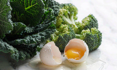 Macro close-up of kale, broccoli florets and a cracked egg on white marble in bright light