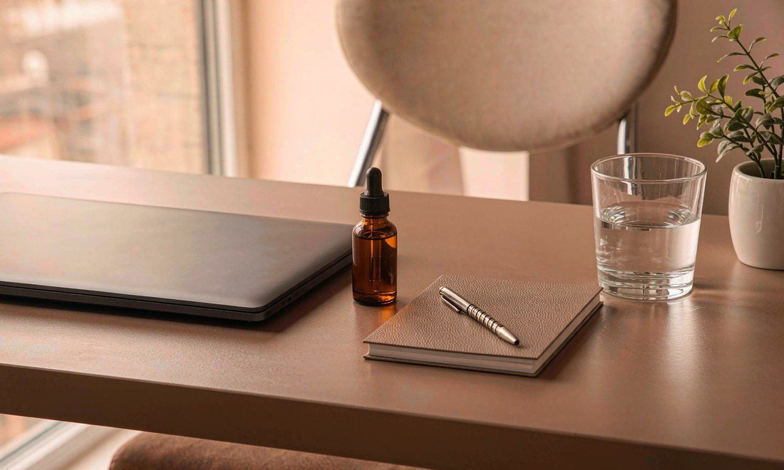 Tidy desk with a small amber dropper bottle, laptop, notebook and water glass in morning light