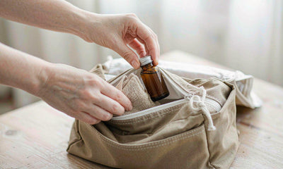Fair-skinned hands packing a small supplement bottle into a canvas travel wash bag in morning light