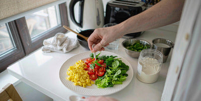 Western fair-skinned hands arranging a breakfast plate of eggs, tomatoes, and greens with a plain jar
