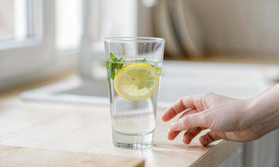 A hand reaching for a glass of lemon and mint water on a sunlit kitchen counter
