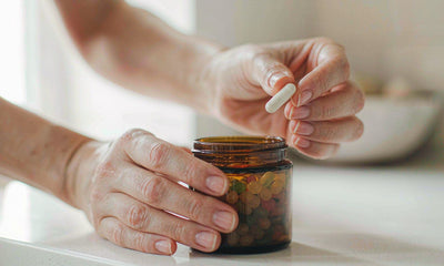 Fair-skinned hands holding a small gummy jar and a single capsule on a clean white kitchen counter