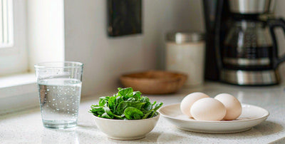 Bright kitchen counter with a glass of water, eggs, and a bowl of greens in soft morning light, no people