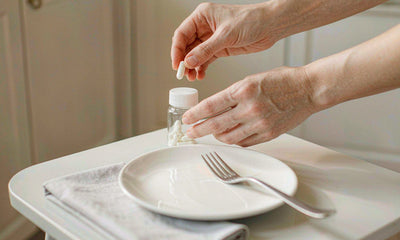 Fair-skinned hands placing a plain capsule bottle beside a single place setting, a simple solo routine