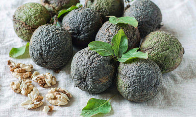Black walnuts in green husks with shelled halves on a light linen cloth