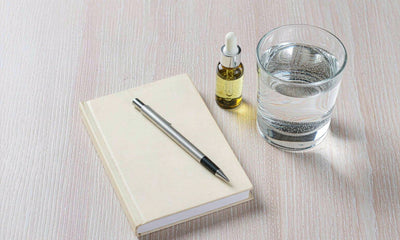Blank notebook, pen, glass of water and an amber dropper bottle on a pale oak desk in soft daylight