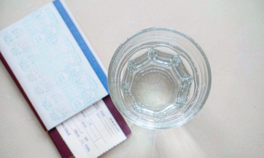 Open passport and boarding pass beside a glass of water on a bright hotel table, travel liver care.