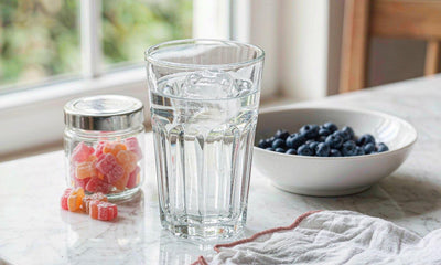 Sunlit kitchen counter with a glass of water, a jar of gummies, blueberries and a linen napkin