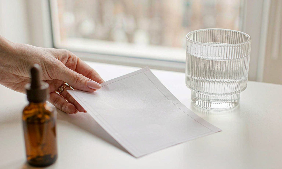 Fair-skinned hand placing a printed blood-test report beside a water glass and a dropper bottle