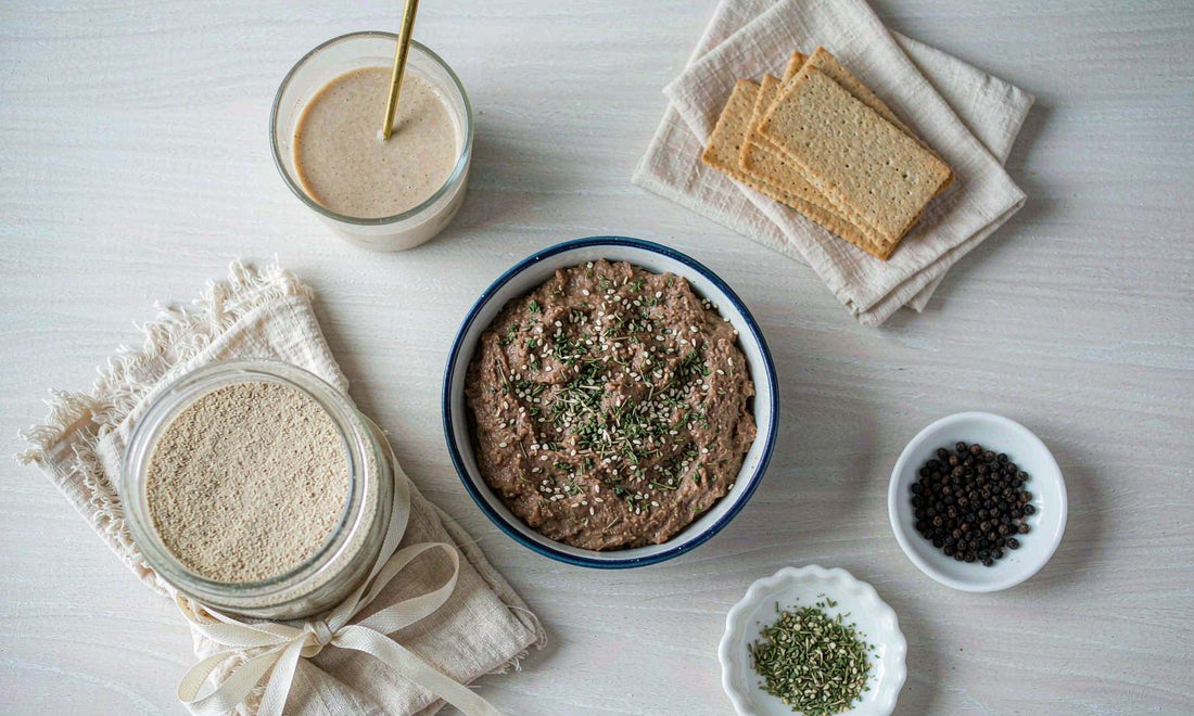 Flat-lay of a plain supplement jar, a bowl of liver pate and crackers on a light wooden table