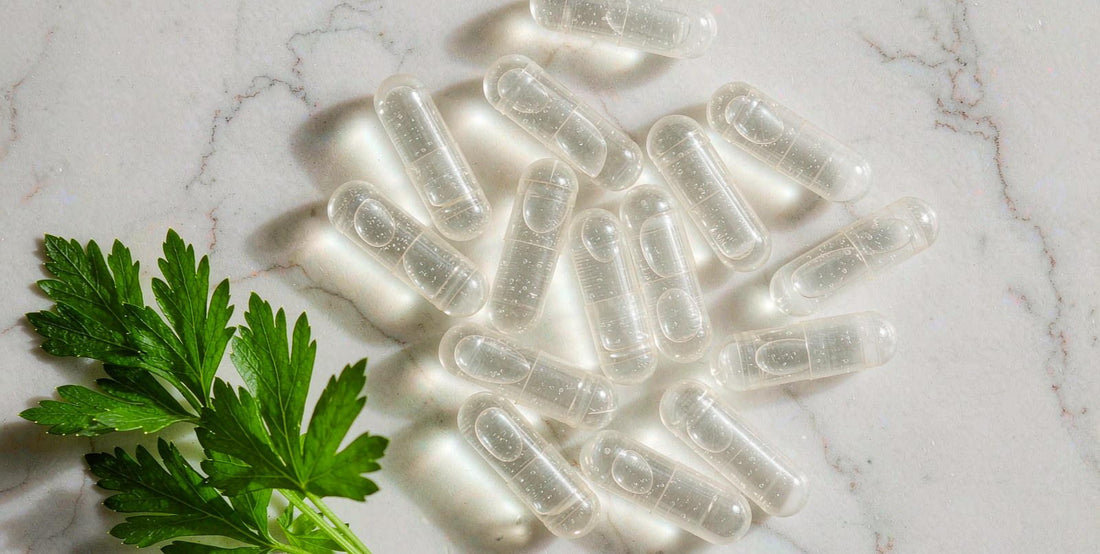 Top-down close-up of plain supplement capsules beside a fresh parsley sprig on white marble