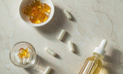Flat lay of amber gummies, plain capsules and a blank dropper bottle on pale stone in soft light