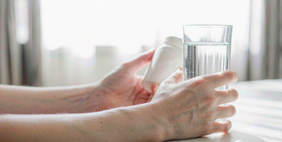 Fair light skin hands holding a plain white bottle beside a glass of clear water