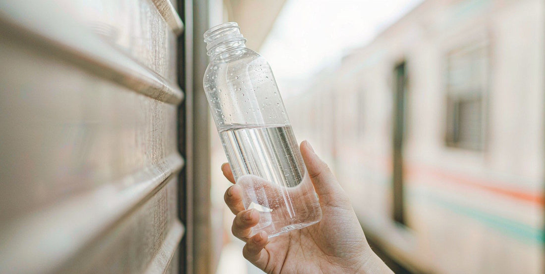 A fair-skinned hand holding a water bottle beside a train window on a shift-change morning