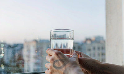 Fair-skinned hands holding a glass of water on a windowsill at dawn after a night shift