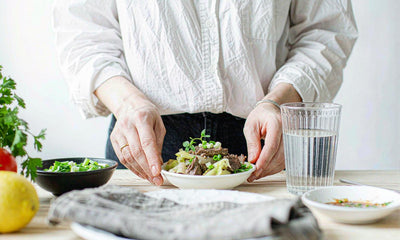 Hands serving a bowl of cooked beef liver with a glass of water on a bright kitchen table