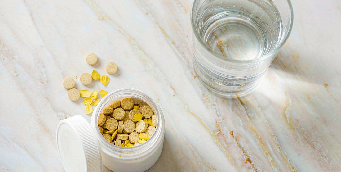 Top-down flat-lay of a plain unlabeled liver tablet jar and a glass of water on bright marble.